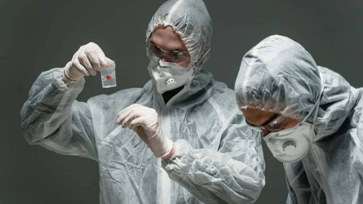 Two scientists in protective suits working in a lab, examining samples safely.