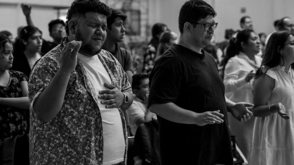 Black and white photo of a diverse religious gathering in Ciudad de México with people engaged in prayer.