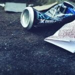 A crumpled beverage can and papers litter an urban street, highlighting environmental issues.