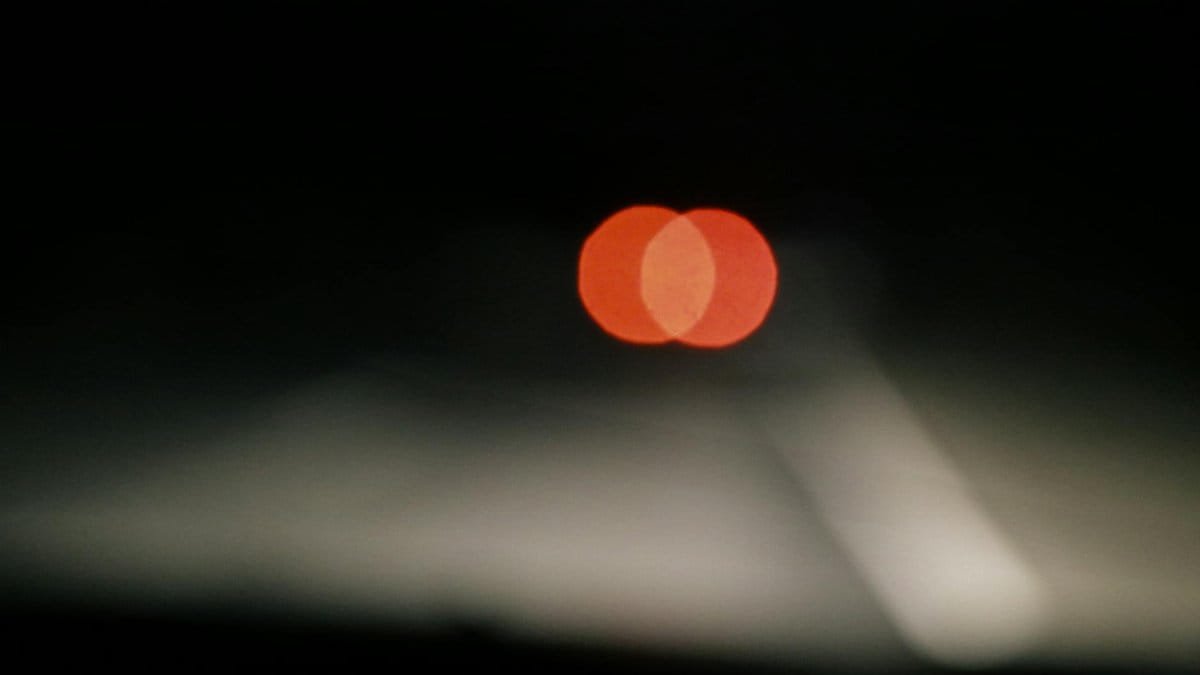 A blurred shot of vehicle tail lights creating a bokeh effect on a dark road night scene.