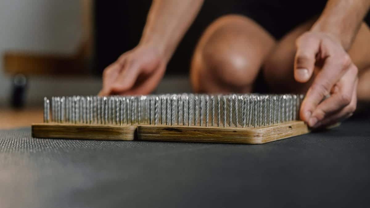 Close-up of hands handling a wooden bed of nails, used for meditation or exercise.