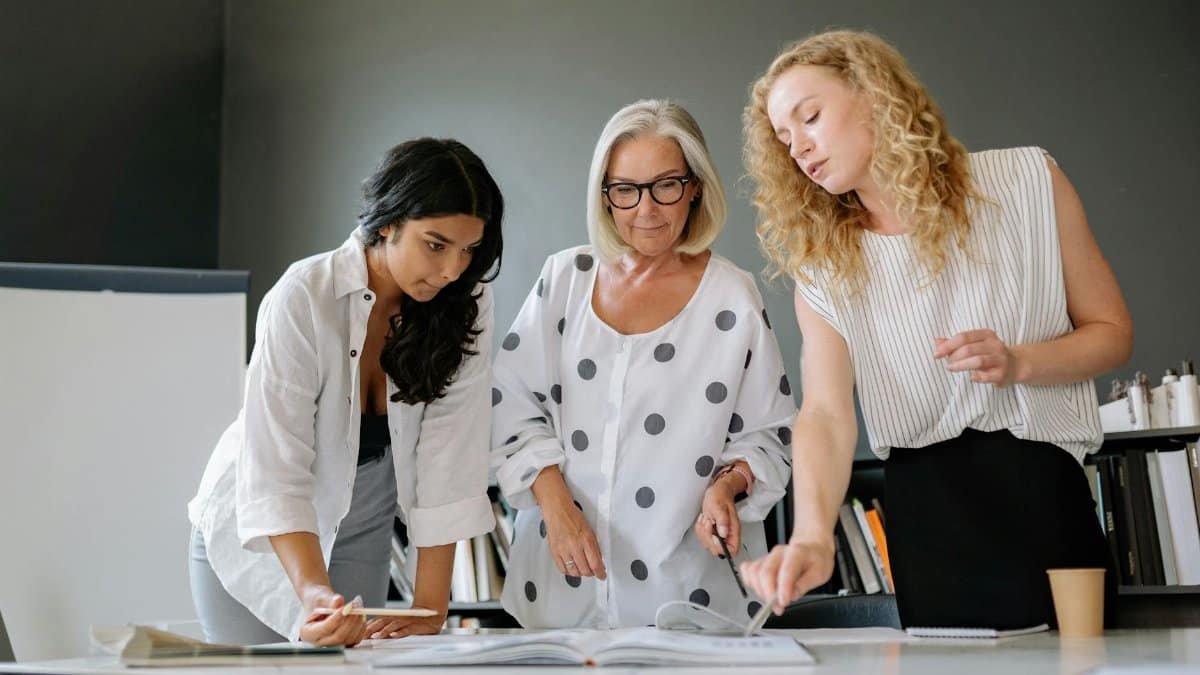 Three professional women collaborating in an office, discussing a document with focus and teamwork.