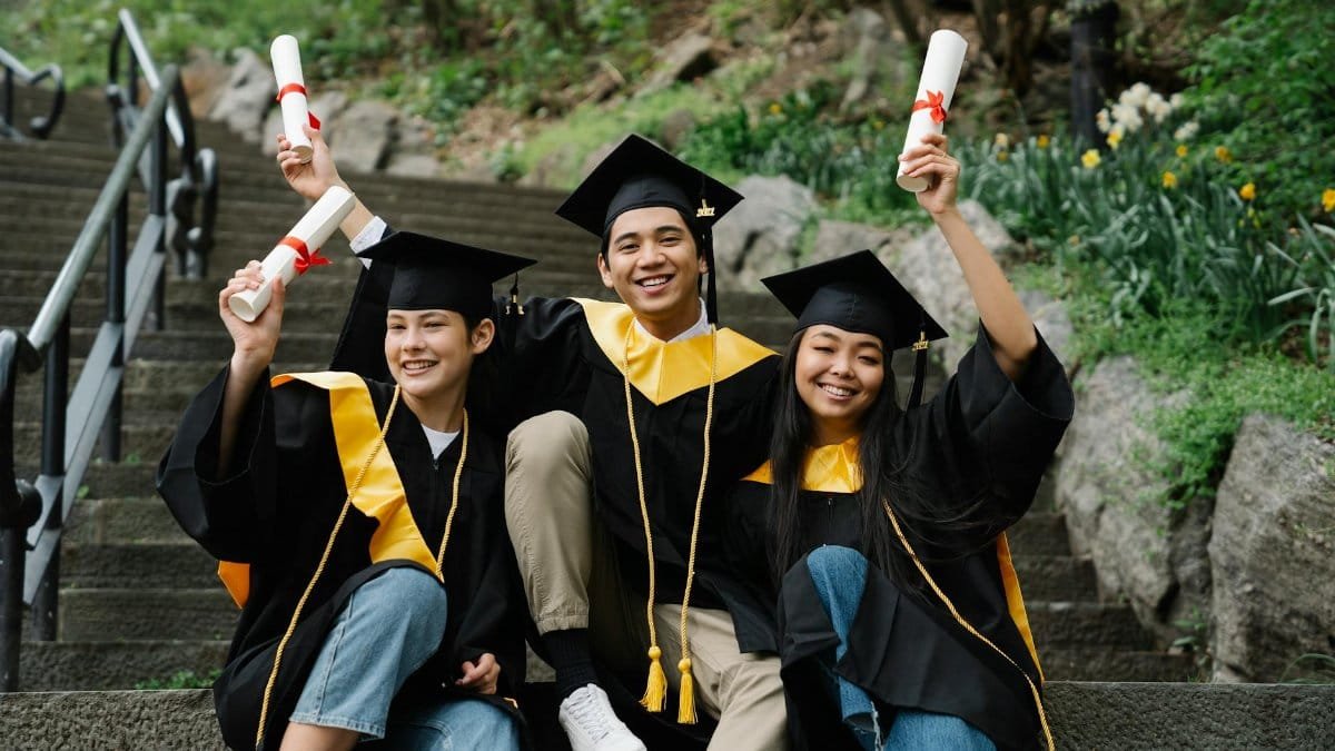 A joyful group of graduates in academic gowns celebrating with diplomas on outdoor steps.