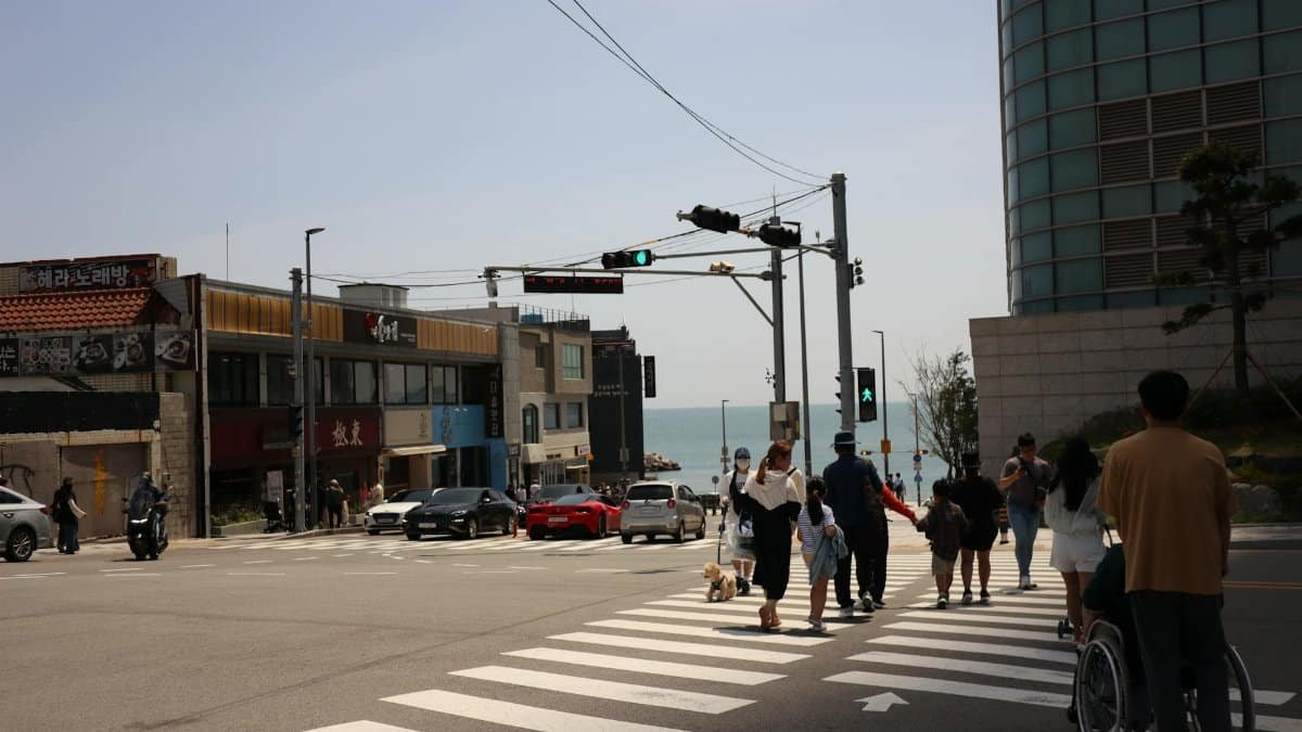 People crossing a busy intersection with a view towards the coastline.
