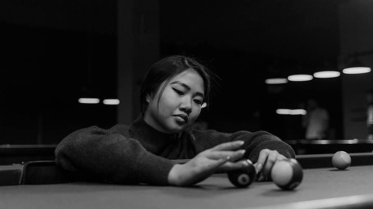 Monochrome image of a woman focusing on billiard balls on a pool table.