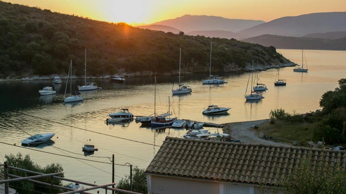 Smooth sea water with floating yachts and green hilly seashore in sunset light