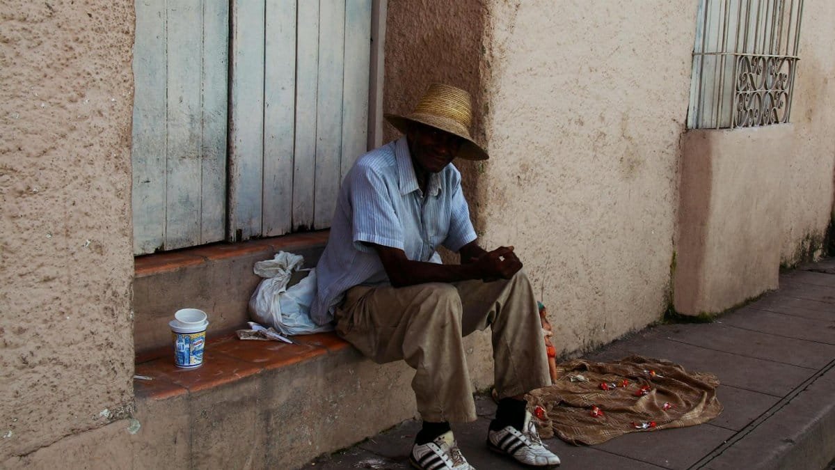 An elderly man in a straw hat sits on a step in a city alley, reflecting urban hardship.