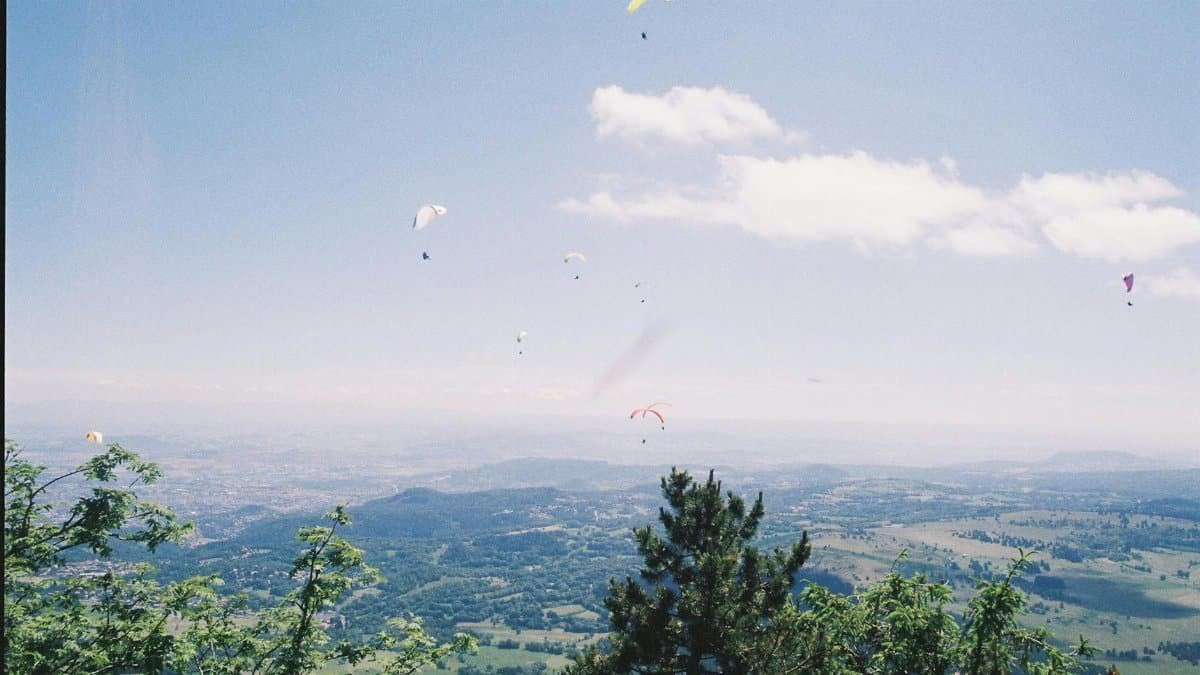 Paragliders soar high above a verdant landscape under a clear blue sky.