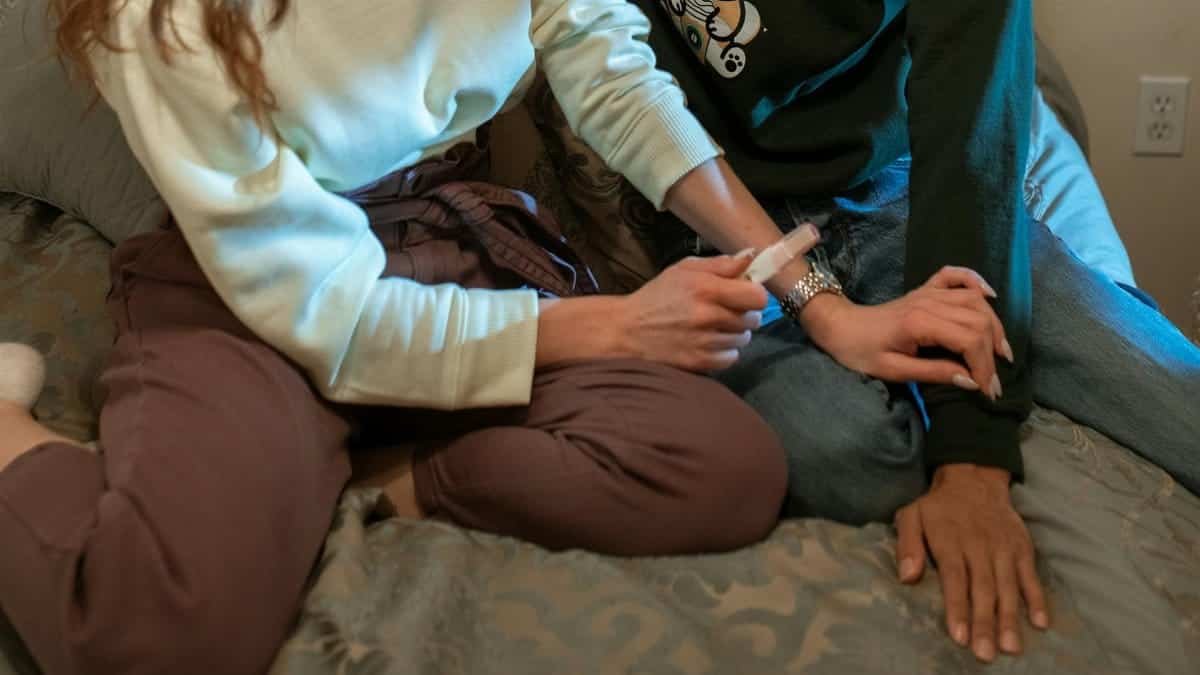 A couple sitting on a bed, sharing a positive pregnancy test result in a cozy, intimate setting.