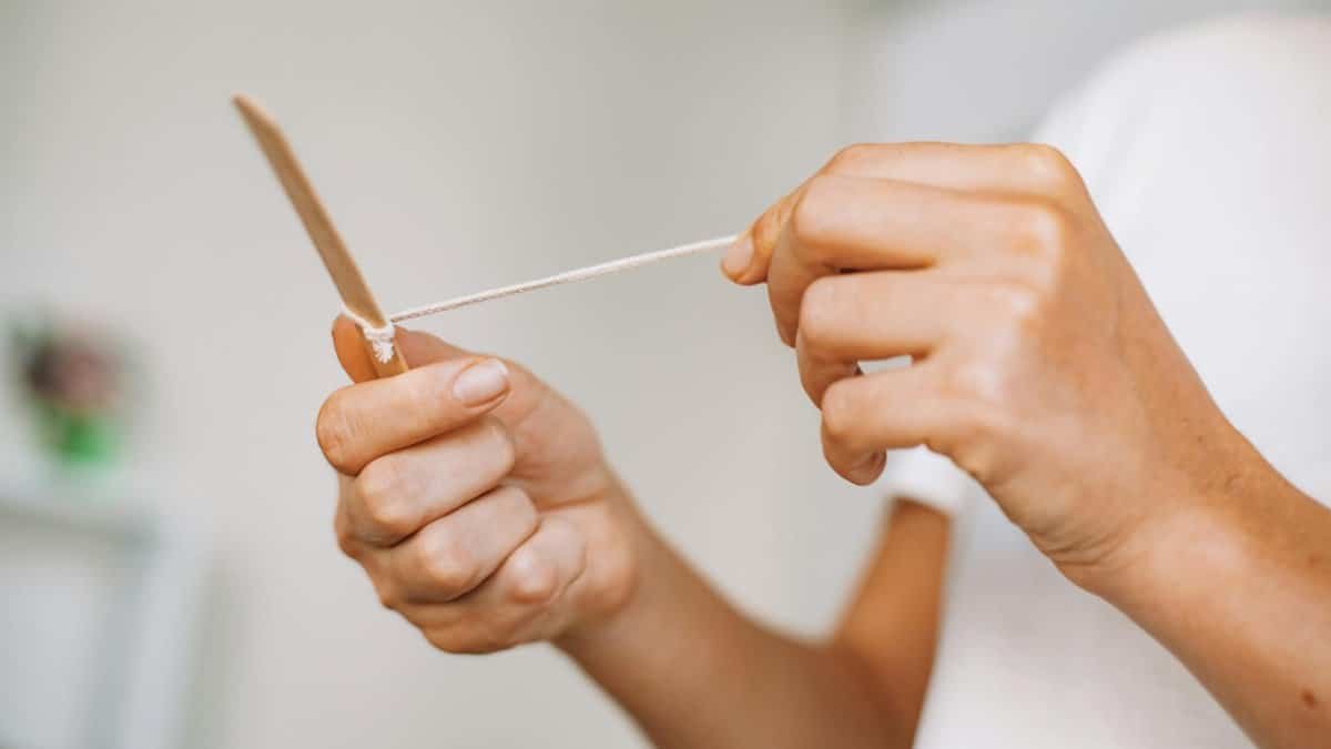 Hands holding a craft stick with string, displaying a creative DIY activity.