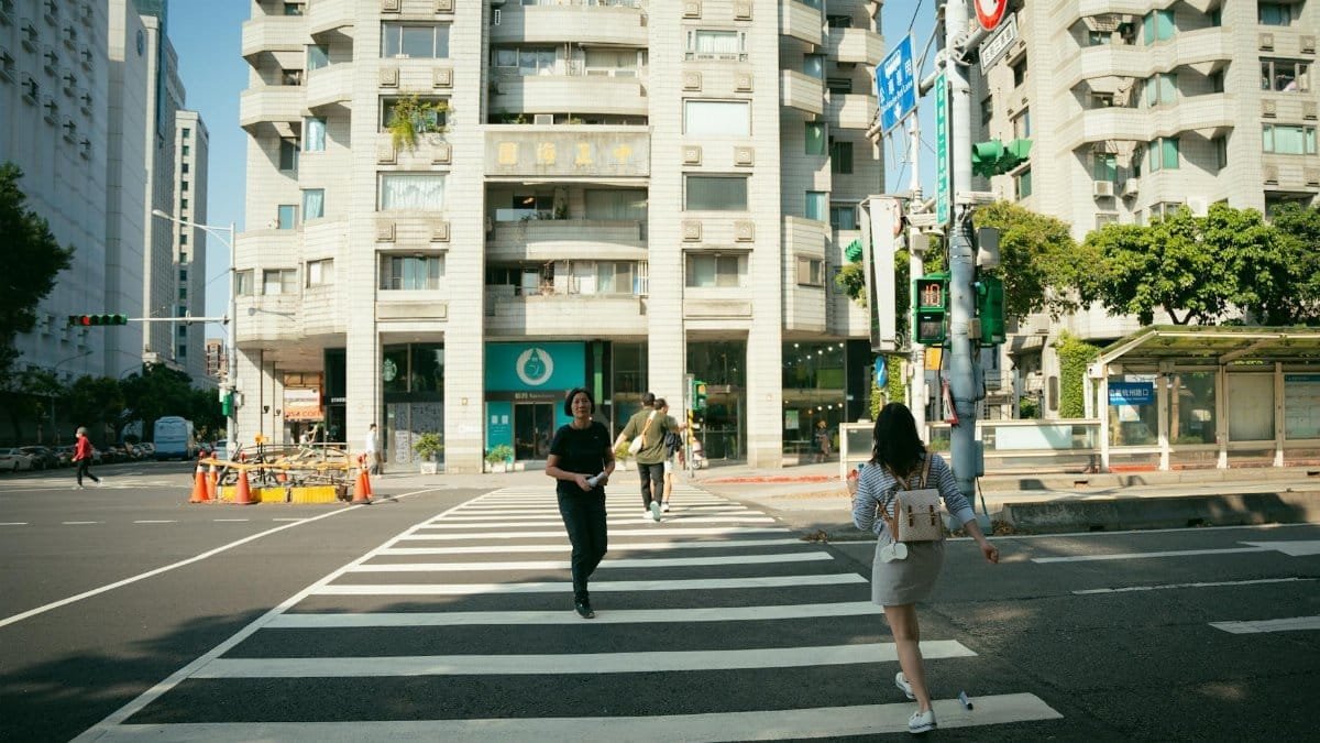 People crossing a crosswalk in a sunny urban street with high-rise buildings.