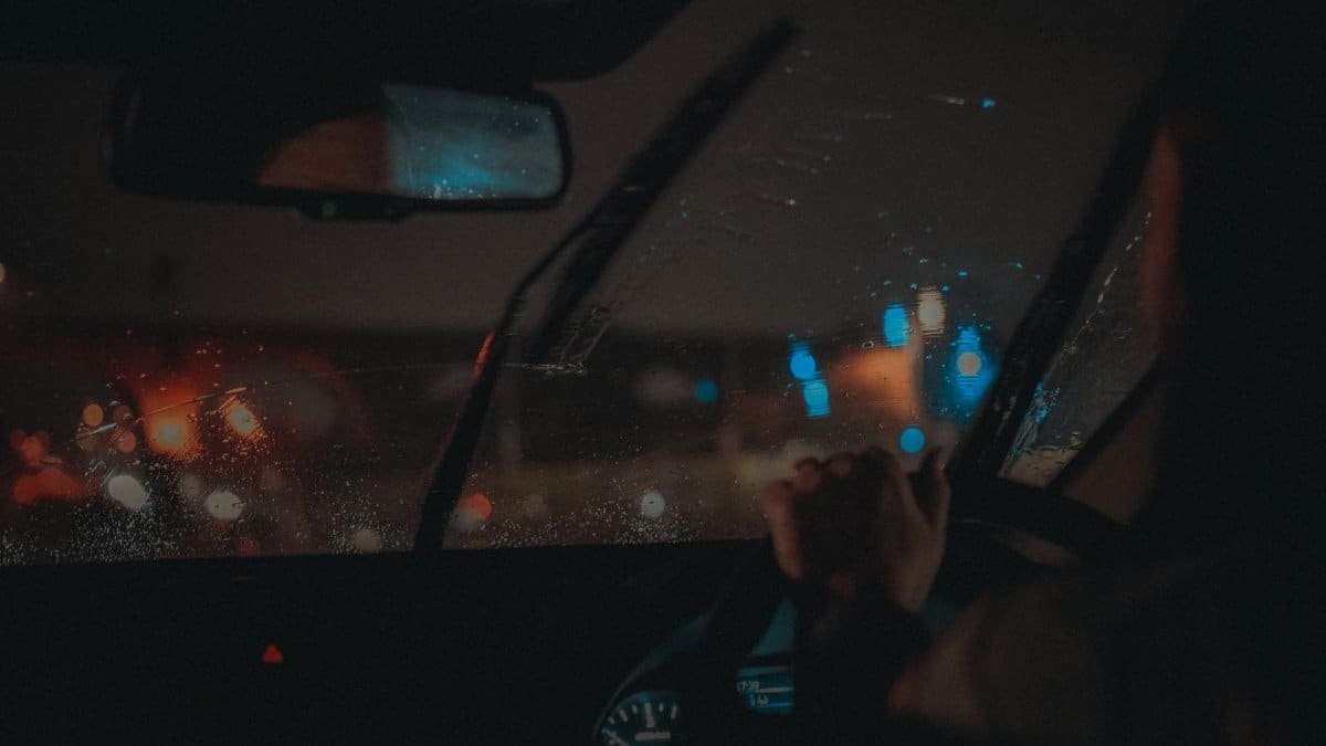 Moody night drive in Manchester with neon lights reflecting on wet windshield.
