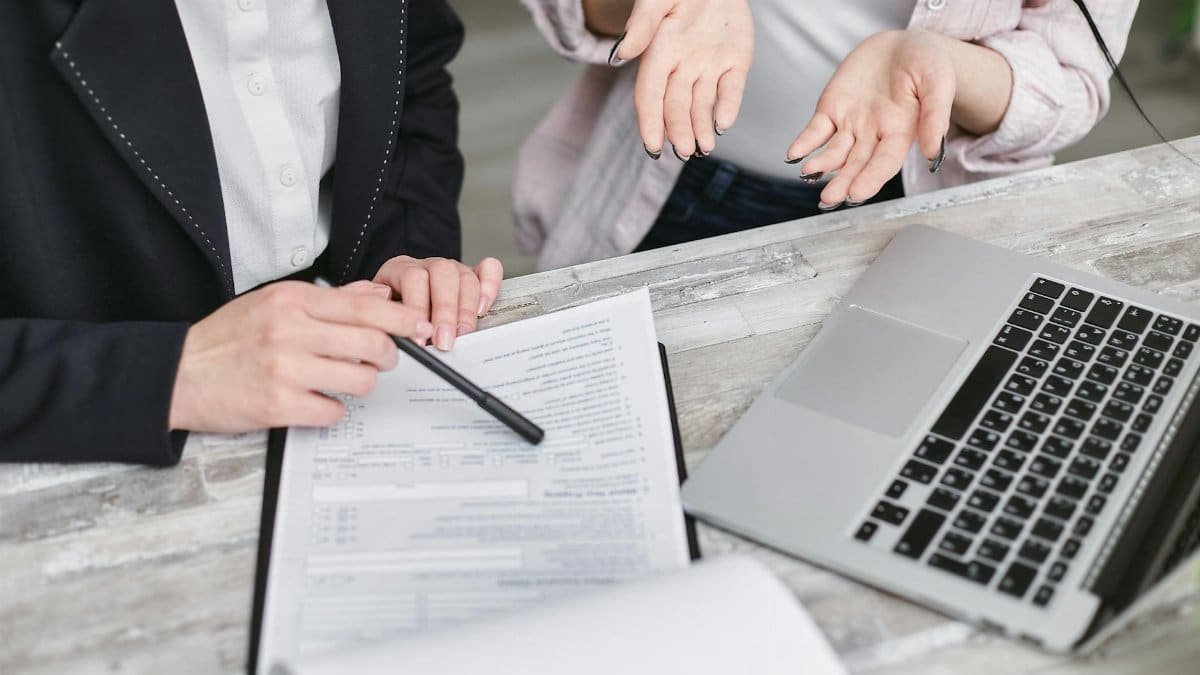 Two professionals discussing a contract at a business meeting with documents and a laptop.