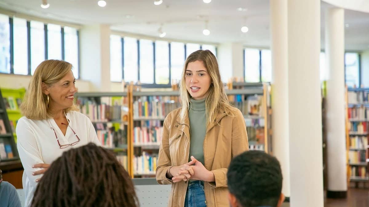 Students and teacher engaged in an active discussion inside a bright university library.