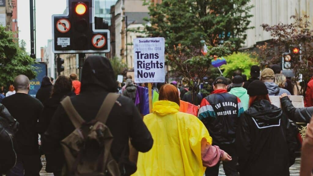 A peaceful transgender rights protest in a city street with participants holding signs and banners.