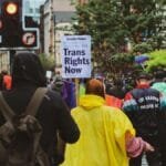 A peaceful transgender rights protest in a city street with participants holding signs and banners.