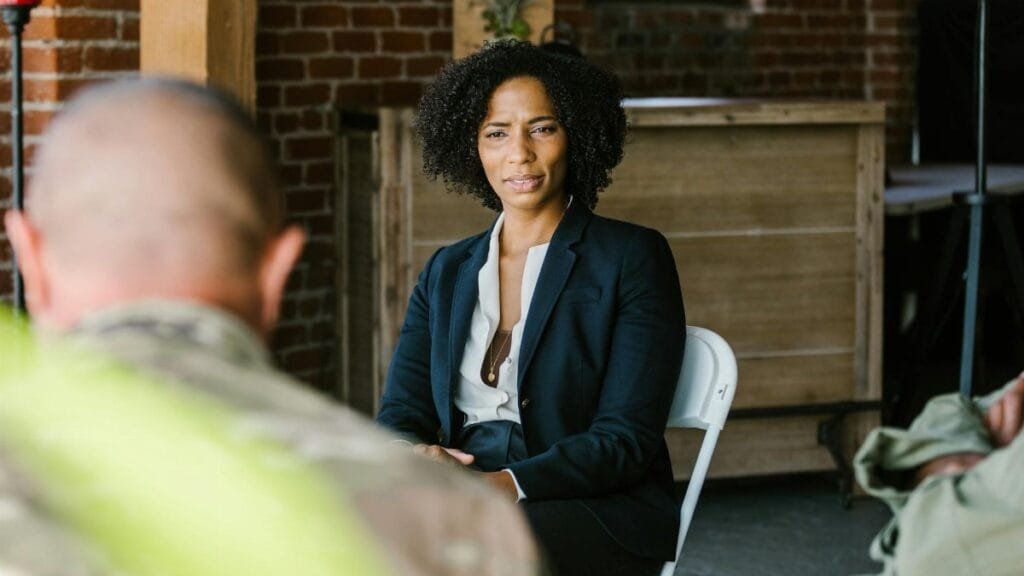 A therapist leads a group therapy session with military veterans in an indoor setting.