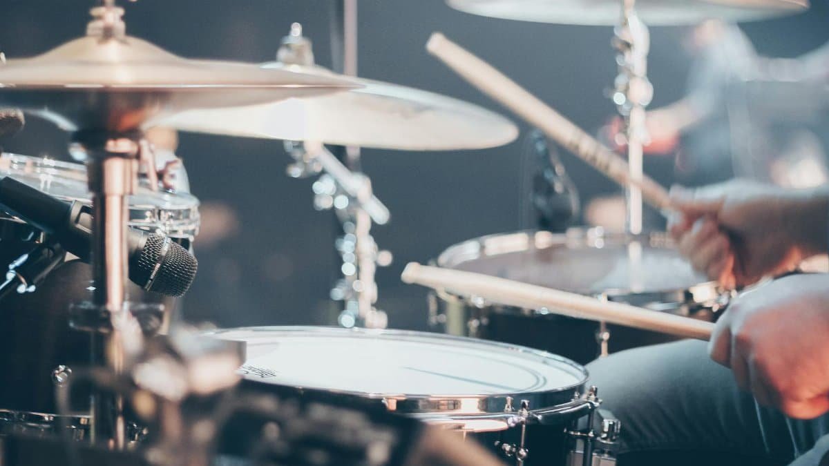 Close-up of a drummer performing on stage with focus on drum set and drumsticks.