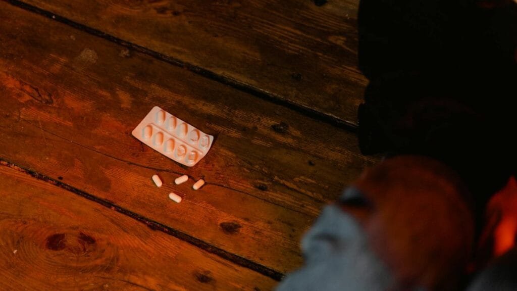 Close-up view of scattered white pills and empty blister pack on a wooden surface, suggesting concepts of medicine or mental health.