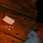 Close-up view of scattered white pills and empty blister pack on a wooden surface, suggesting concepts of medicine or mental health.