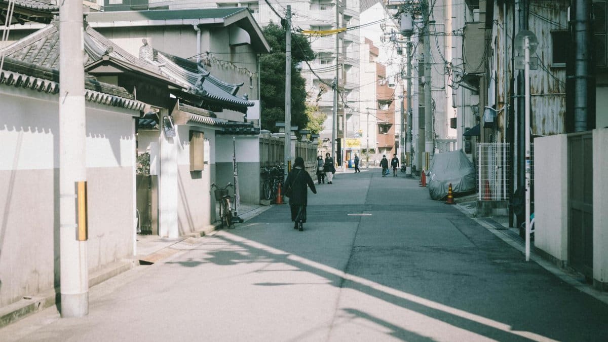 A serene street in Japan with traditional architecture and locals strolling in daylight.