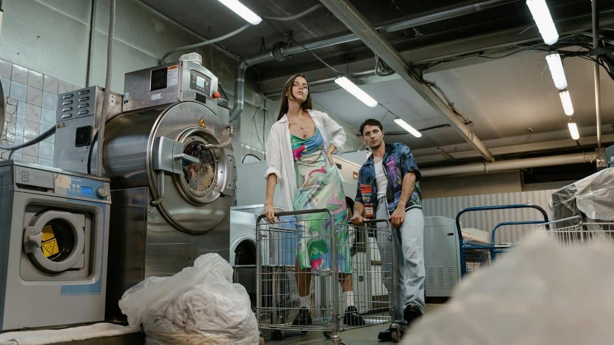 Two adults standing in a laundromat with laundry carts and washing machines, capturing a candid moment.