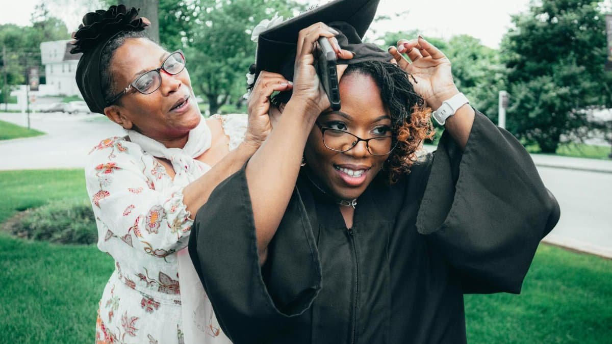A touching moment as a mother helps her daughter with her graduation cap outdoors.