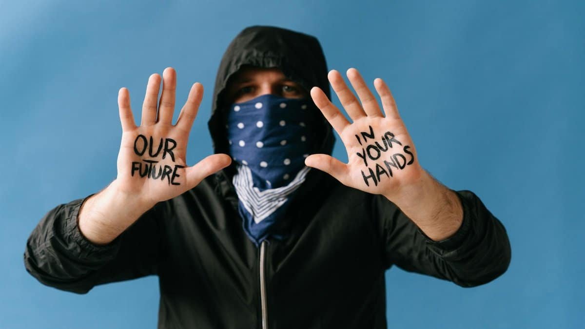 A person wearing a face mask holds hands up with 'OUR FUTURE IN YOUR HANDS' written on them, emphasizing advocacy.