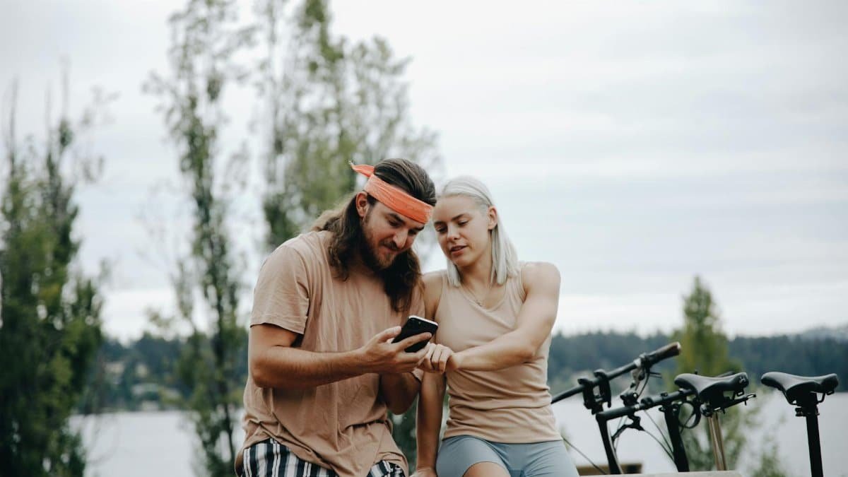 Young couple relaxing outdoors, checking smartphones, enjoying a leisure day in casual sportswear.