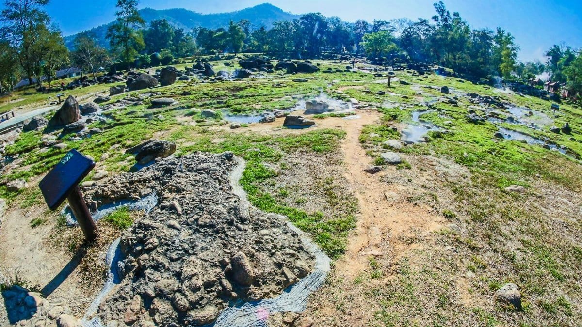 Vibrant landscape featuring natural hot springs with rocks and green patches under a clear sky.