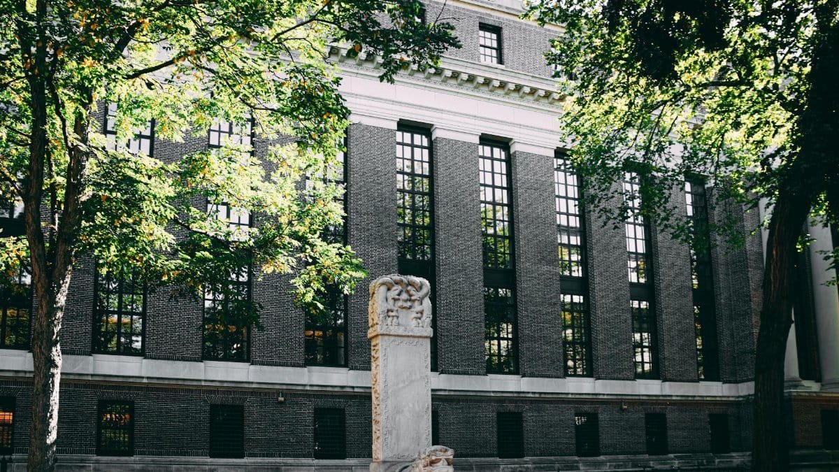 Exterior view of a university building with a stone statue and surrounding trees.