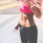 Athletic woman in pink activewear showing toned abs in urban San Francisco setting.