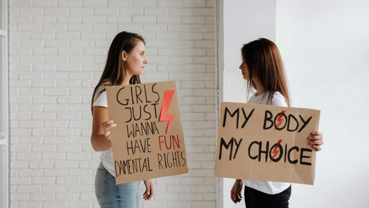 Two women holding protest signs advocating for women's rights indoors.