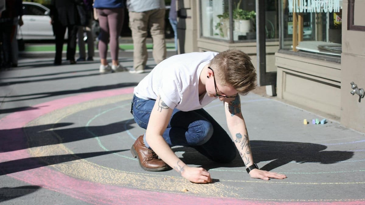A person draws vibrant chalk artwork on urban pavement in Portland, OR.