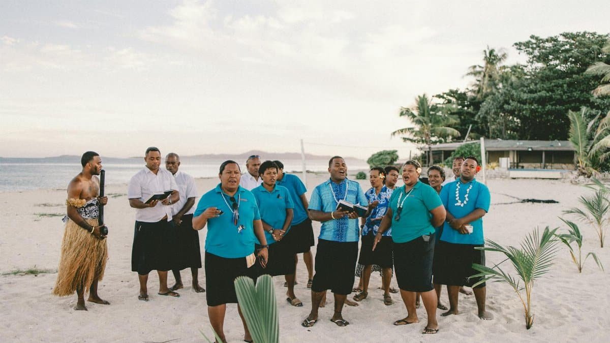 A group of people performing a song on a sandy beach in Nadi, Fiji, showcasing a vibrant cultural gathering.