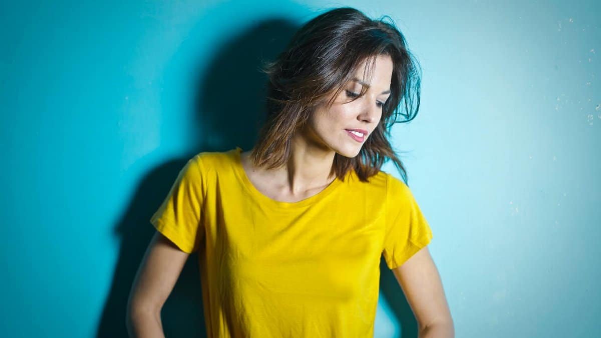 Portrait of a smiling woman in a yellow shirt against a blue wall.