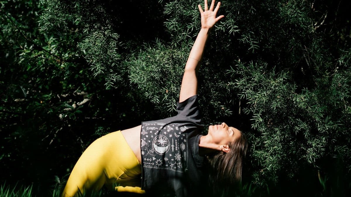 Woman practicing yoga in a peaceful outdoor setting with lush greenery.