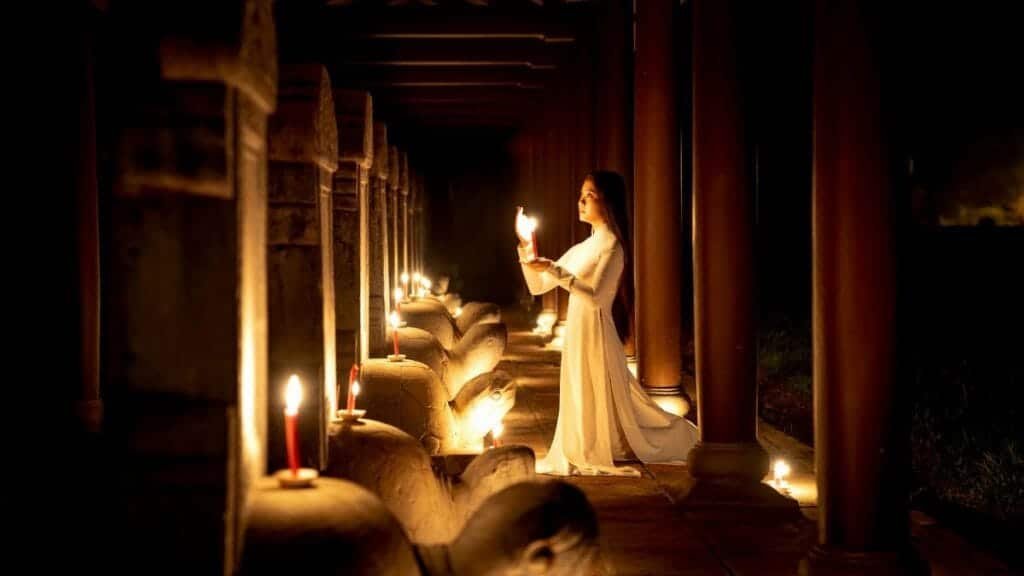 A woman in traditional Ao Dai holding a candle in a dimly lit temple in Hue, Vietnam, creating an atmospheric scene.