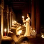 A woman in traditional Ao Dai holding a candle in a dimly lit temple in Hue, Vietnam, creating an atmospheric scene.