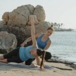 Two women practicing yoga on a beautiful beach during the early morning for fitness and relaxation.