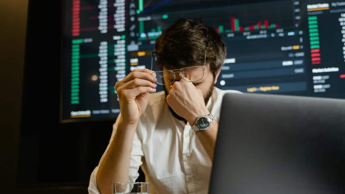 A stressed man looks at stock market data on his computer screen in an office setting.