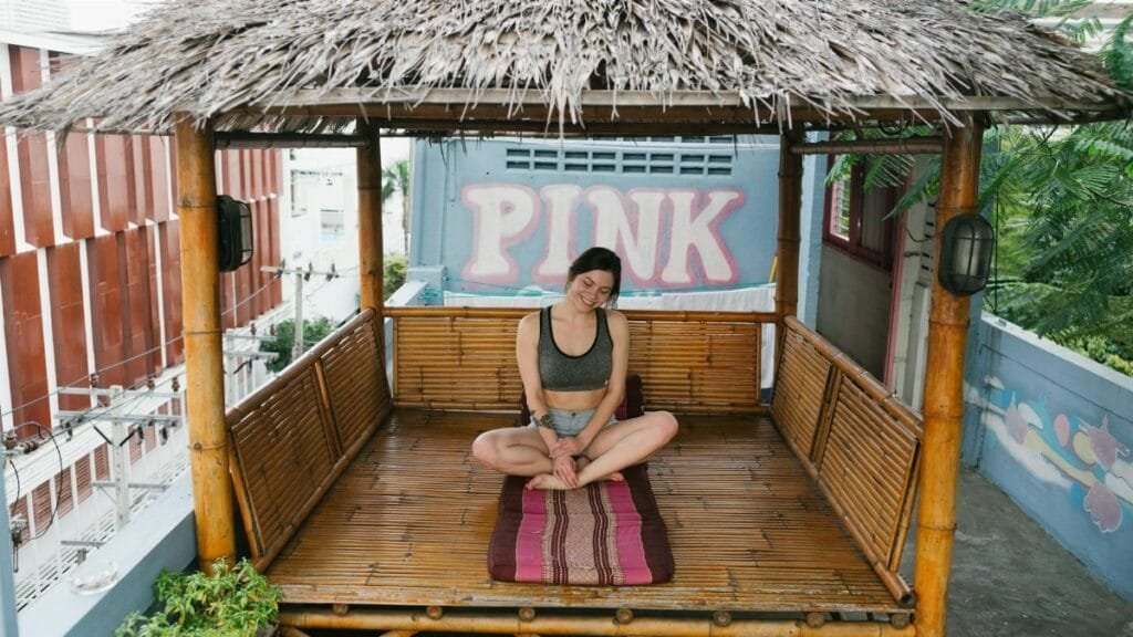A woman practices meditation in a bamboo hut on a rooftop, promoting relaxation amidst urban settings.