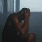 Sweaty man resting on bench in dimly lit locker room, showing exhaustion and recovery.