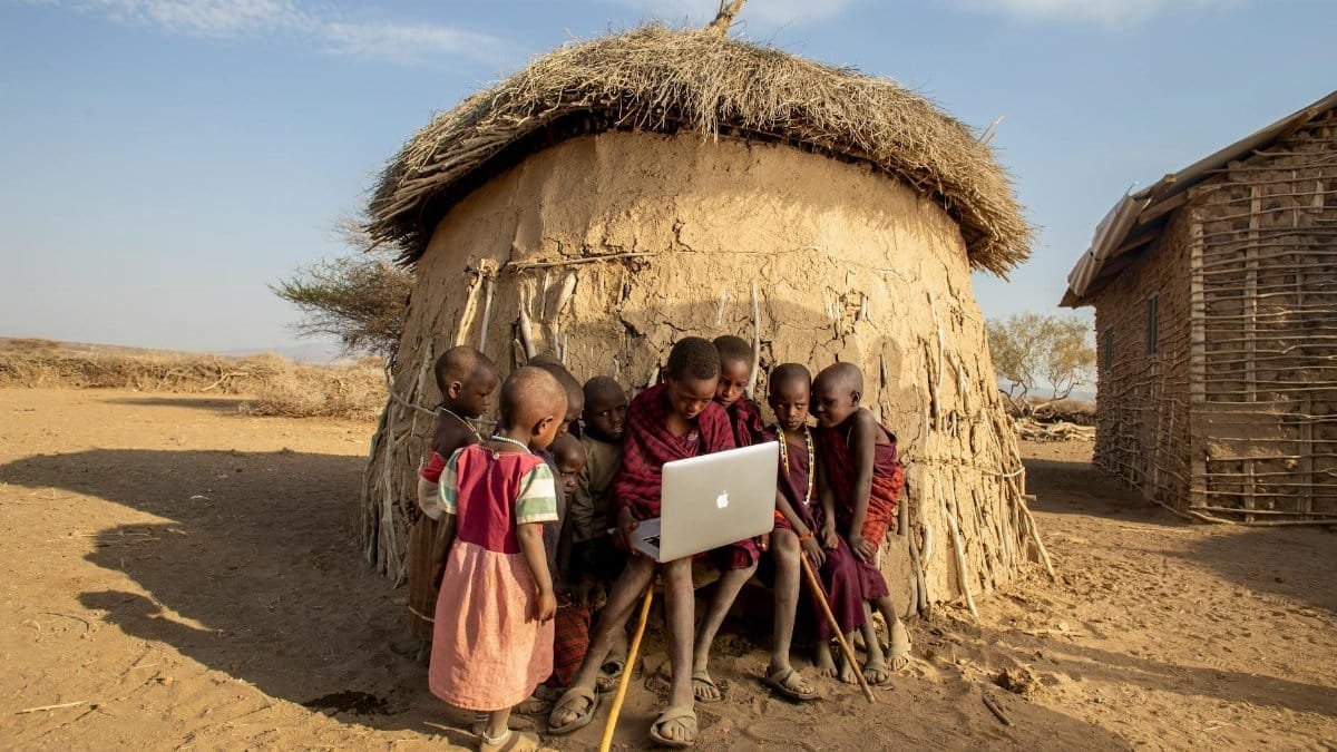Group of African children in a Tanzanian village using a laptop outdoors, engaged in learning.