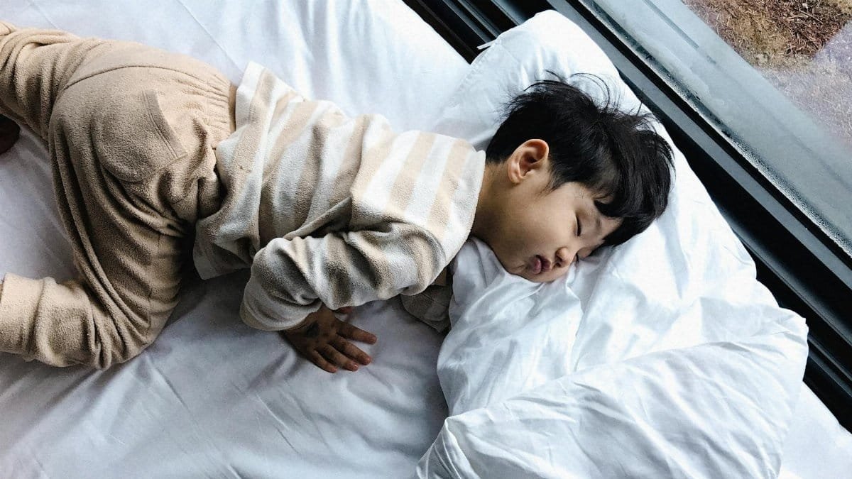 An Asian child peacefully sleeping in cozy pajamas by a window, indoors.