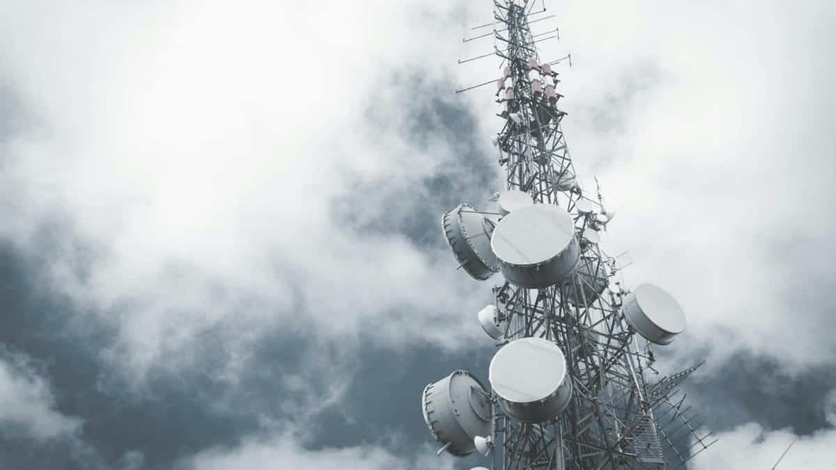 A towering communication mast with satellite dishes, set against a cloudy sky.