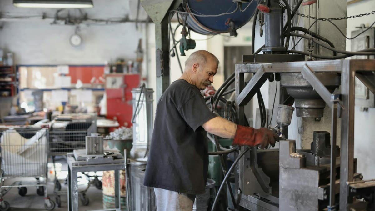 A skilled worker operates heavy machinery in a busy factory environment.