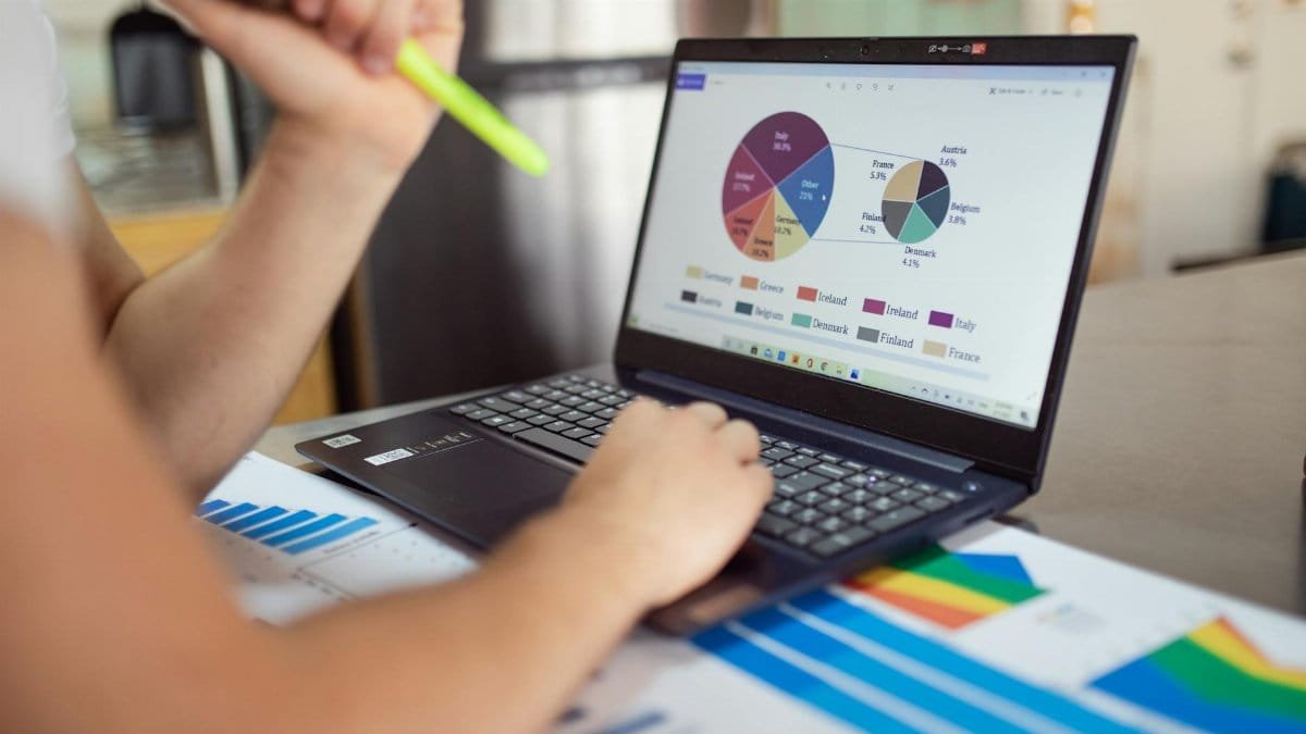 Person analyzing financial charts and graphs on a laptop with colorful documents, showcasing market analysis.
