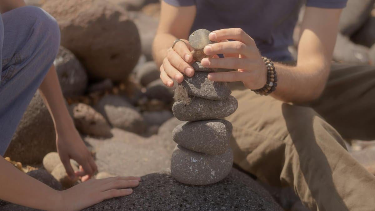 Two people practice mindfulness and balance with stone stacking on a rocky beach.