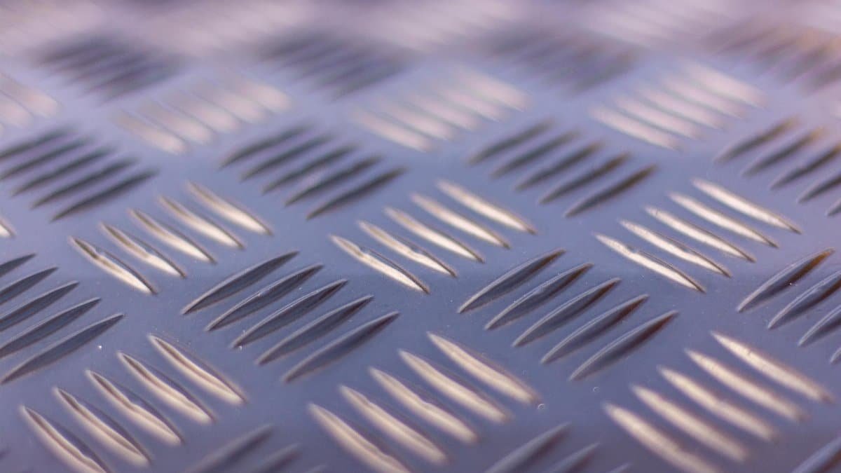 Detailed view of a checker plate metal surface showcasing its ribbed texture in soft lighting.